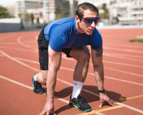 a male athlete squatting ready to sprint on the track wearing Torege sports sunglasses